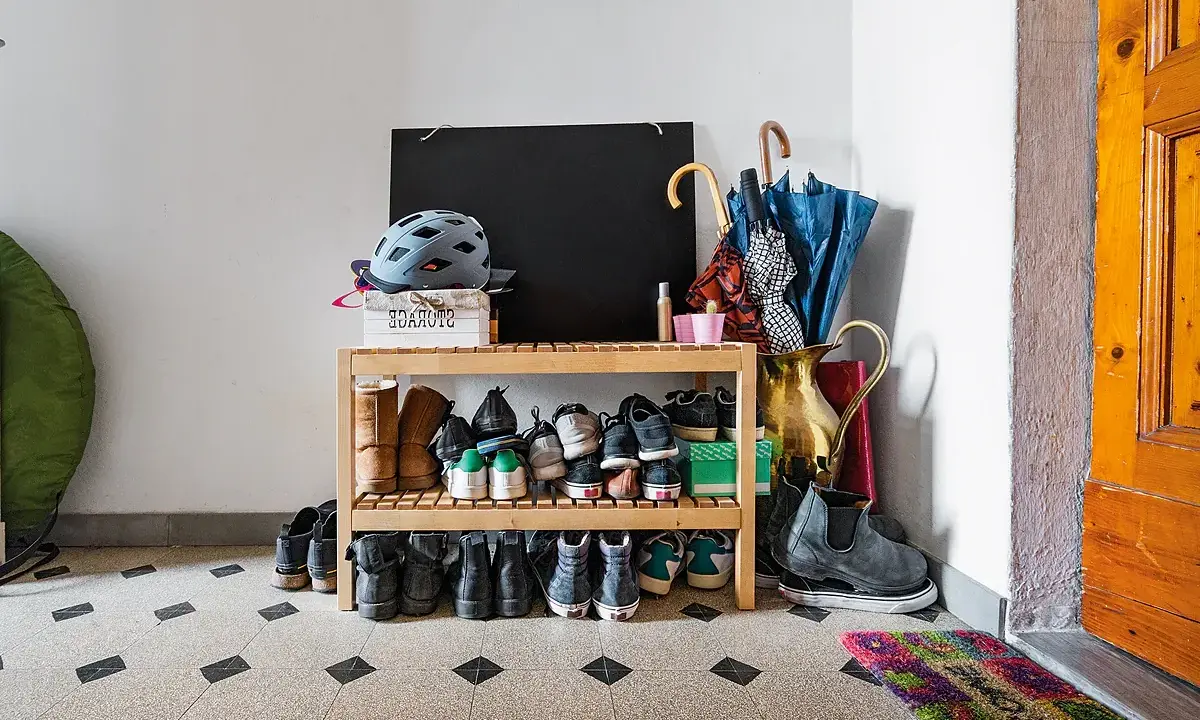 Schuhregal mit vielen Schuhen, Helmen und Regenschirmen im Treppenhaus eines Mehrfamilienhauses.