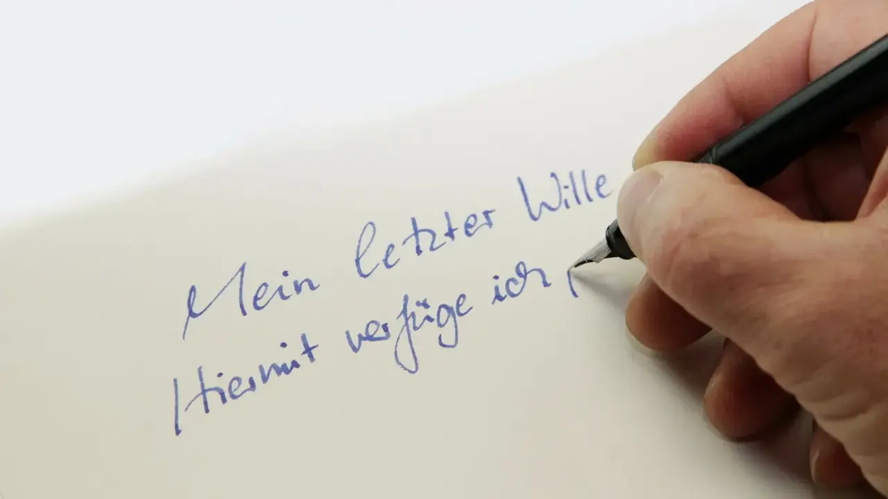 Hand schreibt mit Füllfederhalter auf Papier: "Mein letzter Wille. Hiermit verfüge ich..." – Vorsicht vor Formfehlern bei Testamenten!