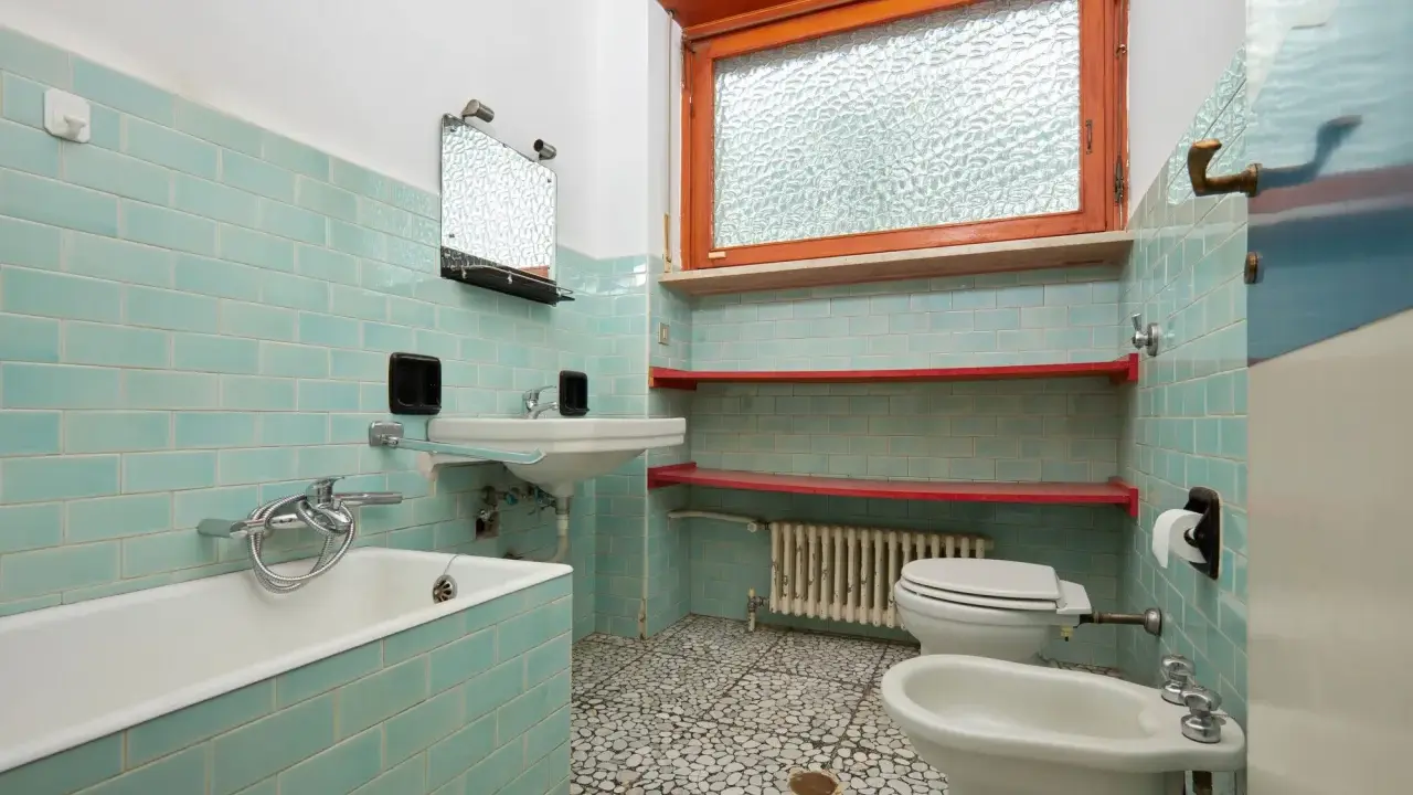 Altes Bad mit türkisen Fliesen, Wanne, Waschbecken, Toilette und Bidet. Hier stellt sich die Frage, wann muss Vermieter Bad renovieren?