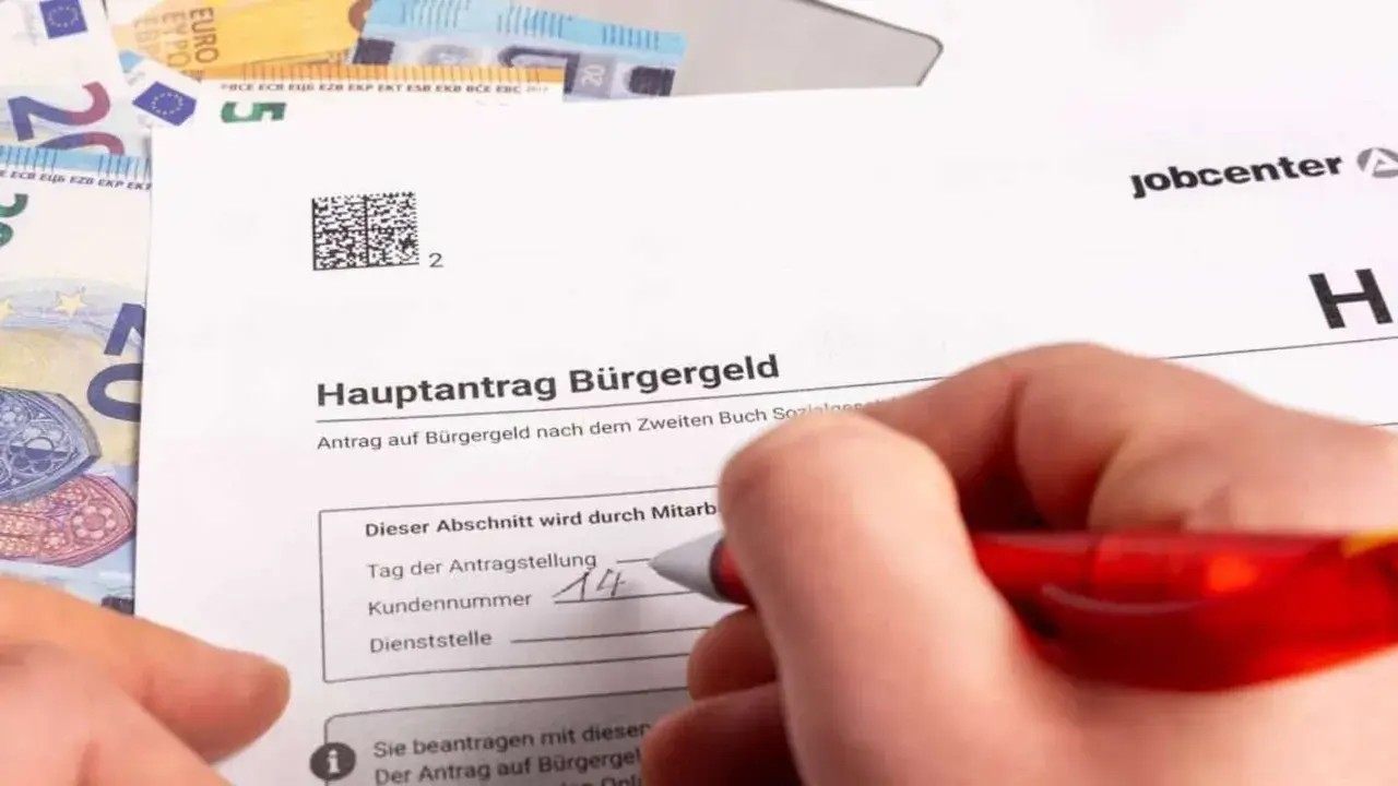 Hand füllt Antrag auf Bürgergeld aus. Geld liegt daneben. Der Antrag betrifft den Selbstbehalt Hartz 4.