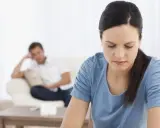 Traurige Frau, Mann im Hintergrund. Die Verwirrung um Trennungsunterhalt und eine mögliche Strafanzeige belastet die Beziehung.