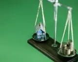 Waage mit Haus und Münzen. Nach einer Scheidung muss eine Hausfrau oft neu planen: Krankenversicherung, Haus und Finanzen neu ordnen.