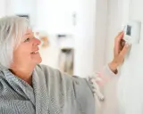 Lächelnde Frau stellt die Heizung auf Nachtabsenkung ein, um Energie zu sparen.