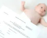 Urkunde zur Vaterschaftsanerkennung liegt neben einem Baby. Die Kosten dafür sind oft gering.