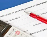 Arbeitsvertrag für geringfügig entlohnte Beschäftigte. Ein roter Stift liegt auf dem Dokument, eine Taschenrechner daneben. Ein 650 Euro Job wird hier geregelt.