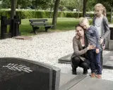 Trauernde Familie am Grab. Die Mutter tröstet ihren Sohn, während die ältere Schwester daneben steht. Sie denken vielleicht an die Zukunft und die halbwaisenrente mindestbetrag.