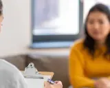Eine Frau im 2. Lehrjahr, schwanger, spricht mit einer Beraterin, die Notizen macht.