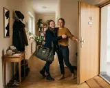 Zwei Freundinnen umarmen sich freudig im Flur. Die Frage "wie lange darf jemand bei mir wohnen ohne anmeldung" beschäftigt viele.