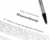 Hausordnung für ein Mehrfamilienhaus, Anlage zum Mietvertrag. Ein Stift liegt auf dem Dokument.