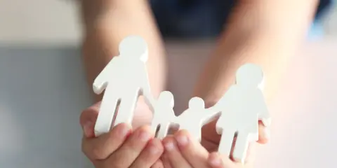 Hände halten weiße Figuren einer Familie. Mögliche Nachteile beim gemeinsamen Sorgerecht werden hier symbolisch dargestellt.