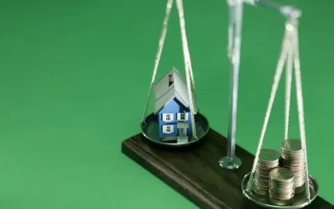 Waage mit Haus und Münzen. Nach einer Scheidung muss eine Hausfrau oft neu planen: Krankenversicherung, Haus und Finanzen neu ordnen.