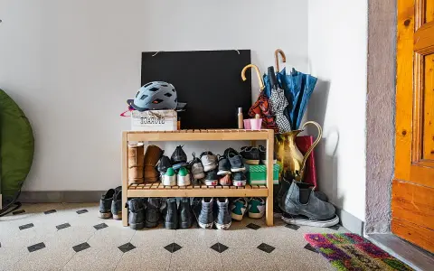 Schuhregal mit vielen Schuhen, Helmen und Regenschirmen im Treppenhaus eines Mehrfamilienhauses.