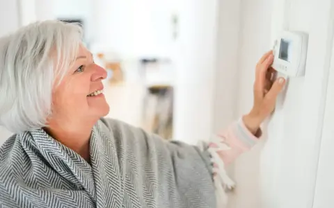 Lächelnde Frau stellt die Heizung auf Nachtabsenkung ein, um Energie zu sparen.