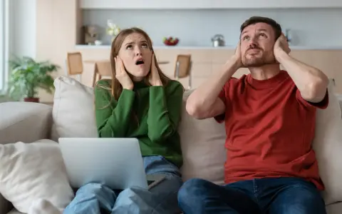 Genervtes Paar auf dem Sofa, Hände an den Ohren. Seit die Mittagsruhe BW abgeschafft ist, ist es hier nie mehr ruhig.