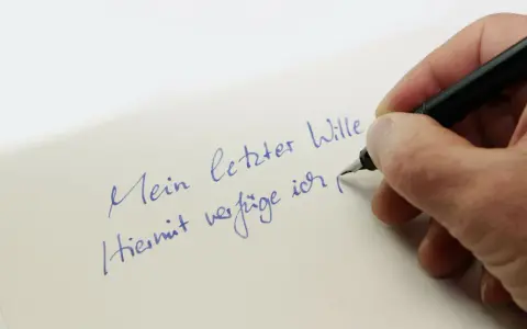 Hand schreibt mit Füllfederhalter auf Papier: "Mein letzter Wille. Hiermit verfüge ich..." – Vorsicht vor Formfehlern bei Testamenten!