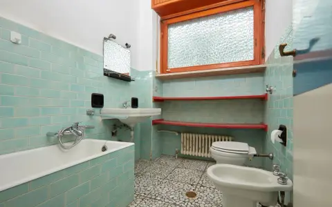 Altes Bad mit türkisen Fliesen, Wanne, Waschbecken, Toilette und Bidet. Hier stellt sich die Frage, wann muss Vermieter Bad renovieren?
