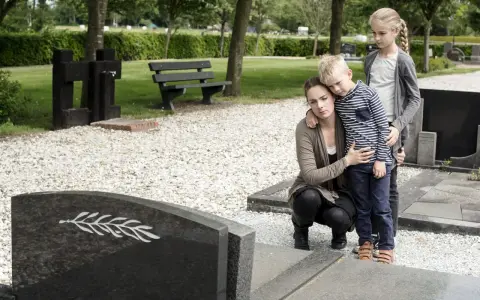 Trauernde Familie am Grab. Die Mutter tröstet ihren Sohn, während die ältere Schwester daneben steht. Sie denken vielleicht an die Zukunft und die halbwaisenrente mindestbetrag.