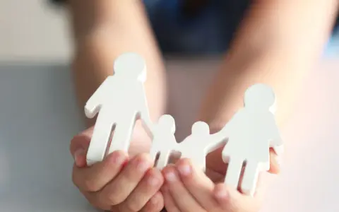 Hände halten weiße Figuren einer Familie. Mögliche Nachteile beim gemeinsamen Sorgerecht werden hier symbolisch dargestellt.