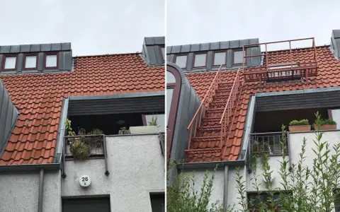 Brandschutz Dachboden Mehrfamilienhaus: Rote Metalltreppe führt zu einem Dachfenster. Dachziegel und Gauben sind sichtbar.