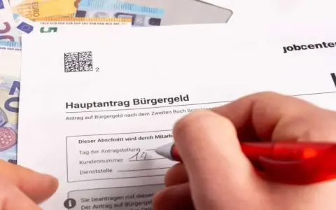Hand füllt Antrag auf Bürgergeld aus. Geld liegt daneben. Der Antrag betrifft den Selbstbehalt Hartz 4.