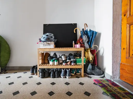 Schuhregal mit vielen Schuhen, Helmen und Regenschirmen im Treppenhaus eines Mehrfamilienhauses.