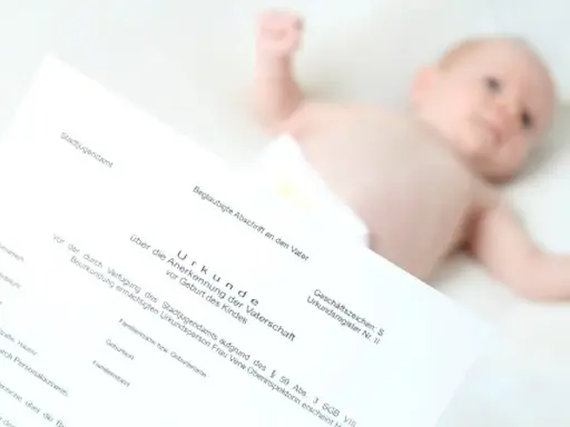 Urkunde zur Vaterschaftsanerkennung liegt neben einem Baby. Die Kosten dafür sind oft gering.