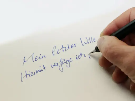 Hand schreibt mit Füllfederhalter auf Papier: "Mein letzter Wille. Hiermit verfüge ich..." – Vorsicht vor Formfehlern bei Testamenten!