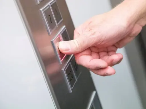 Da der Aufzug defekt ist, drückt die Hand den Knopf für die Mietminderung.