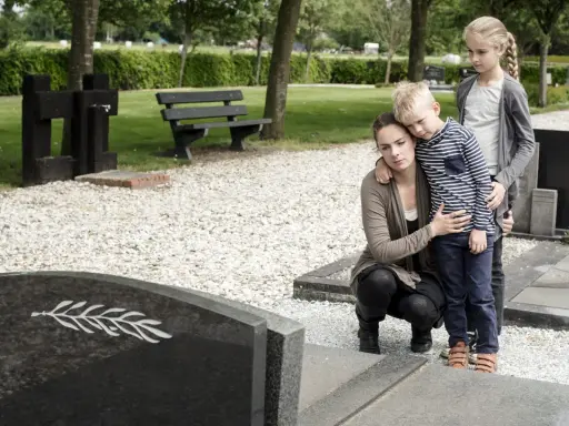 Trauernde Familie am Grab. Die Mutter tröstet ihren Sohn, während die ältere Schwester daneben steht. Sie denken vielleicht an die Zukunft und die halbwaisenrente mindestbetrag.