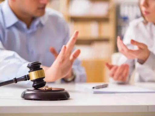 Streit um die Scheidungsfolgenvereinbarung: Ein Paar diskutiert vor einem Richterhammer mit Eheringen.