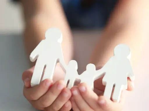 Hände halten weiße Figuren einer Familie. Mögliche Nachteile beim gemeinsamen Sorgerecht werden hier symbolisch dargestellt.