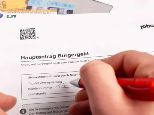 Hand füllt Antrag auf Bürgergeld aus. Geld liegt daneben. Der Antrag betrifft den Selbstbehalt Hartz 4.