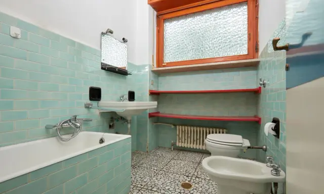 Altes Bad mit türkisen Fliesen, Wanne, Waschbecken, Toilette und Bidet. Hier stellt sich die Frage, wann muss Vermieter Bad renovieren?