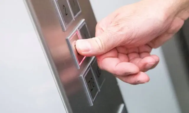 Da der Aufzug defekt ist, drückt die Hand den Knopf für die Mietminderung.