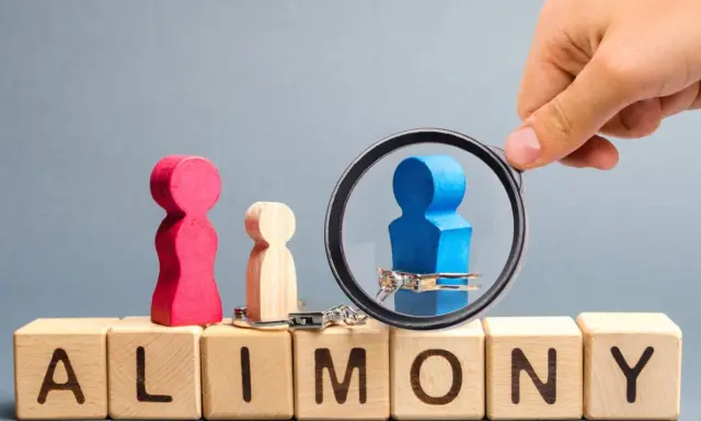 Holzfiguren und Handschellen auf Würfeln mit "ALIMONY". Ein blauer Mann unter Lupe, der Unterhaltsschulden und Privatinsolvenz symbolisiert, die das Jugendamt betreffen.