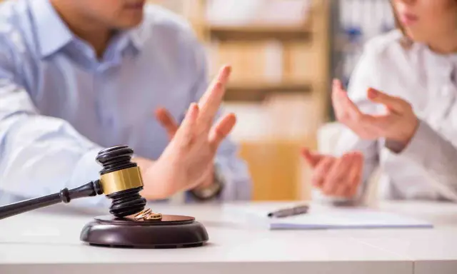 Streit um die Scheidungsfolgenvereinbarung: Ein Paar diskutiert vor einem Richterhammer mit Eheringen.
