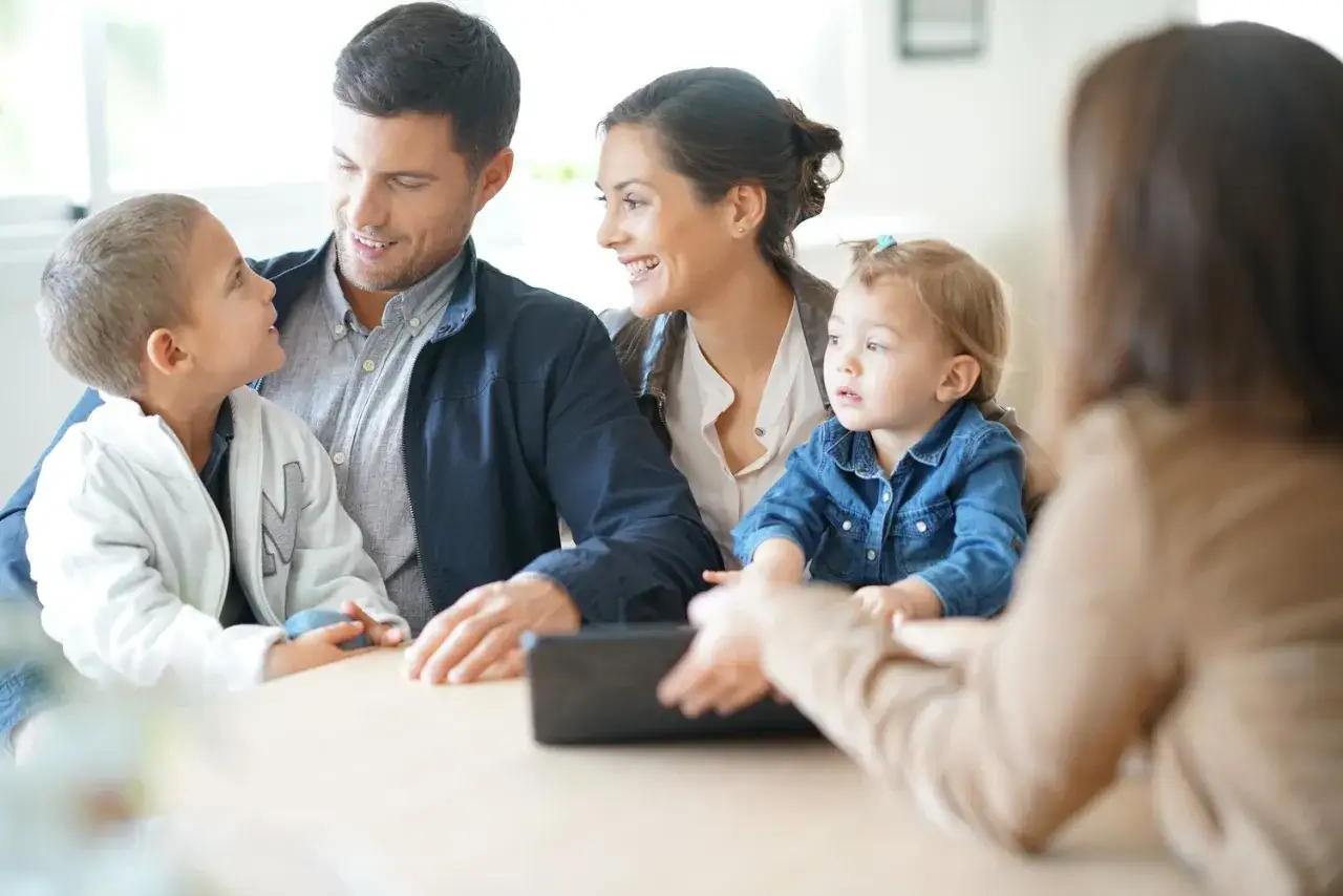 Familie im Gespräch, vielleicht über einen Antrag auf Hilfe zur Erziehung. Vater, Mutter und zwei Kinder sitzen am Tisch.