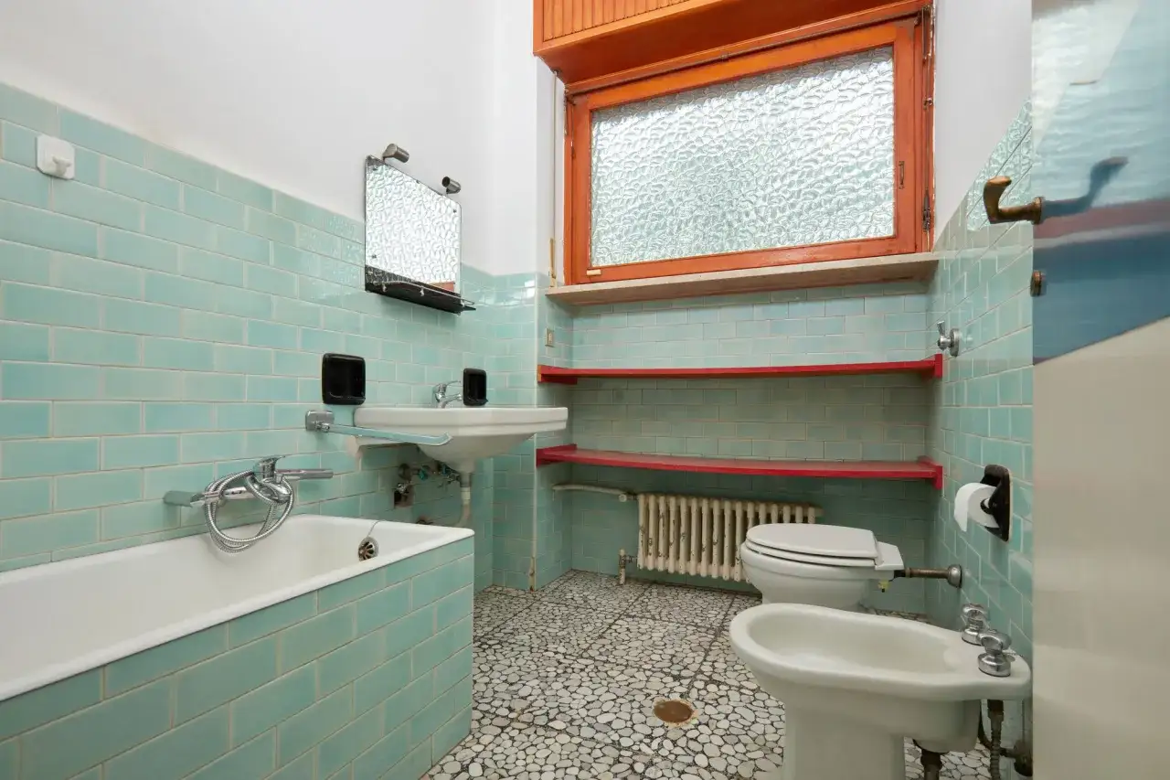 Alt-Text: Ein veraltetes Badezimmer mit hellblauen Kacheln, einer Badewanne, einem Waschbecken, Toilette und Bidet. Wann muss Vermieter Bad renovieren? Hier ist ein Beispiel für ein Bad, das eine Auffrischung nötig hat.
