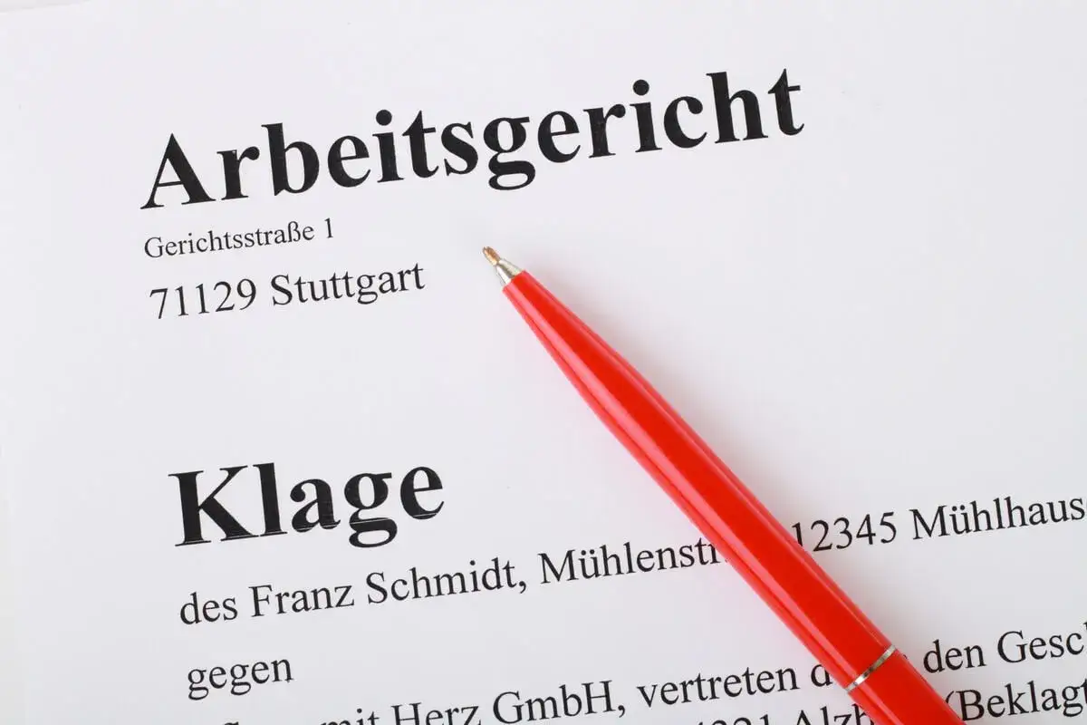 Ein roter Stift liegt auf einem Dokument des Arbeitsgerichts Stuttgart. Es handelt sich um eine Klageschrift, die 5 kschg. erwähnt.