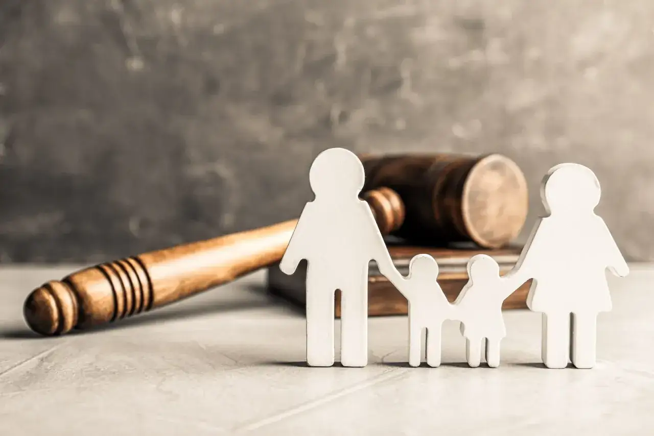Familienfiguren vor einem Richterhammer. Bei Nichtzahlung des Trennungsunterhalts droht eine Strafanzeige.