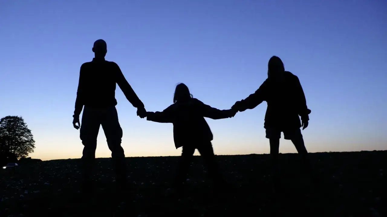 Drei Silhouetten halten Händchen im Abendhimmel. Ein Mann, ein Kind und eine Frau, die den selbstbehalt mit Kind im Haushalt symbolisieren.