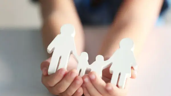 Hände halten weiße Figuren einer Familie. Mögliche Nachteile beim gemeinsamen Sorgerecht werden hier symbolisch dargestellt.